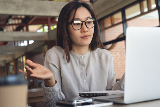 Confused asian businesswoman gesturing while using laptop in cafe, remote work problem solving concept.