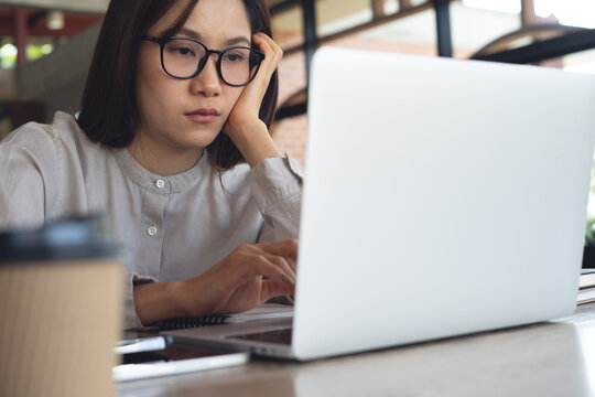 Close up of a burned-out asian woman sitting at cafe, staring at her laptop with low energy, low motivation burnout cobcept
