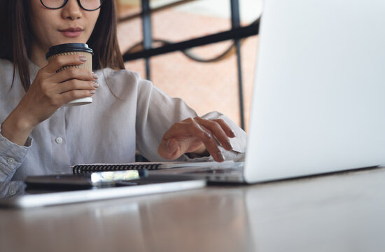 Asian business woman working on laptop while drinking coffee in cafe, modern workspace, focused remote work, online business concept.
