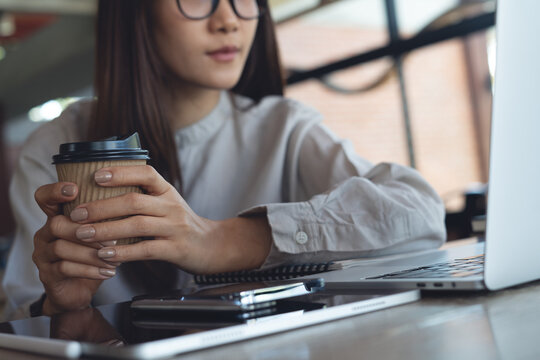Asian businesswoman working on laptop while drinking coffee in cafe, modern workspace, focused remote work, online business concept.