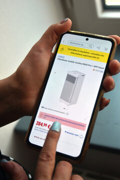 St- Amand Montrond - France - 5 August 2026 - Editorial detail of a woman's hands using a smartphone while browsing portable air conditioners on the Lidl website, illustrating online shopping 
