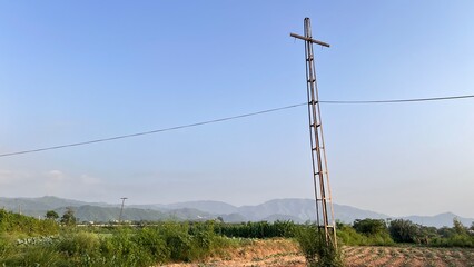 Wooden cross on utility pole in rural landscape with clear blue sky for religious or travel themes. © Ai HUB