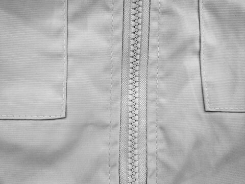 Close up of closed plastic zipper on grey fabric jacket with pocket stitching. Textile detail background.