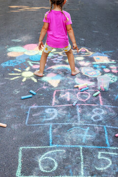 Little girl playing hopscotch drawn with chalk on asphalt