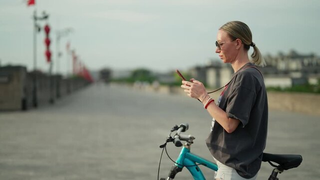 Tourist woman with rental bicycle in Beijing, travel and tourism, use smartphone . Active female traveler looking at electronic map in mobile phone, people riding bikes in city center in summer