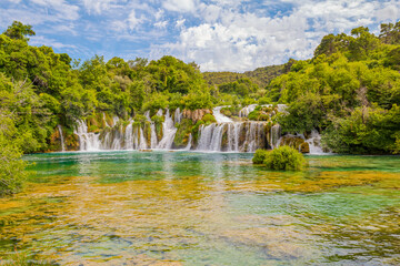 Krka National Park, Croatia, view of the Krka waterfall on a sunny day, featuring cascading water, lush greenery, wooden walkways, and a stunning natural landscape in bright Mediterranean light. © johnkruger1