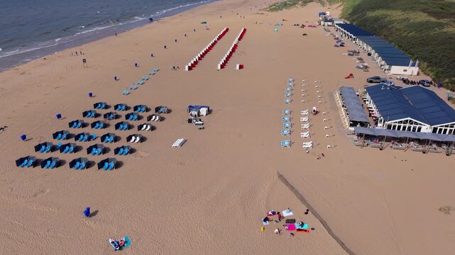 Aerial view video clip of Katwijk aan Zee beach resort, beach chairs, windbreak screens, beach cabins, restaurant pavilion, and North Sea shore in South Holland, Netherlands on a sunny day