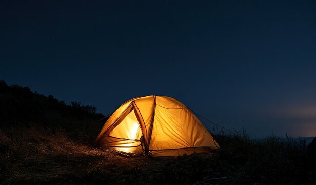 Lit tent glows warmly on a dark, grassy hillside under a starlit sky