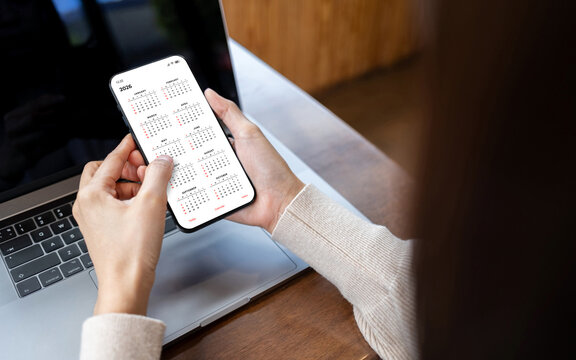 Young woman using smartphone with monthly calendar to plan 2026 activities. Scheduling and organizing plans. Technology and business concept.
