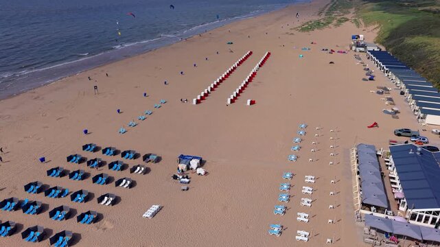Aerial view video clip of Katwijk aan Zee beach resort blue sun loungers red beach cabins windbreak screens seaside restaurant sand dunes and North Sea shore in South Holland Netherlands on sunny day