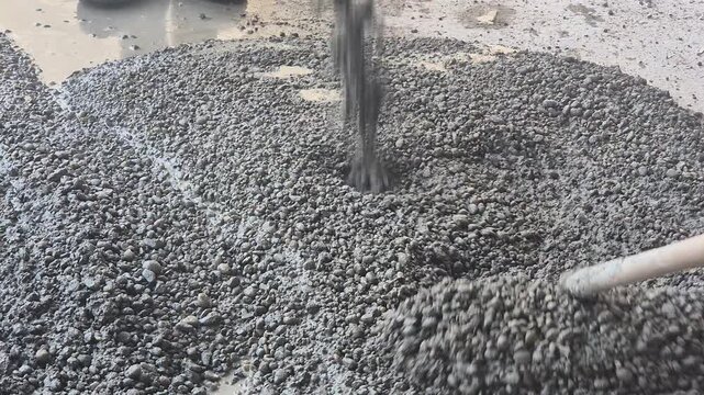 Construction workers using rakes to spread and shape coarse aggregate concrete for a slope formation.