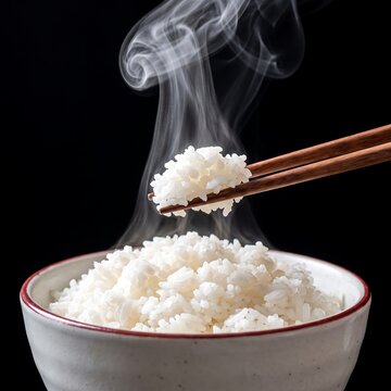 Steaming bowl of freshly cooked white rice with chopsticks, closeup a warm, fluffy portion of rice being lifted with wooden chopsticks against a black background