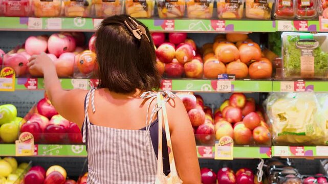 Asian Woman Selecting Fresh Apples in Supermarket Aisle