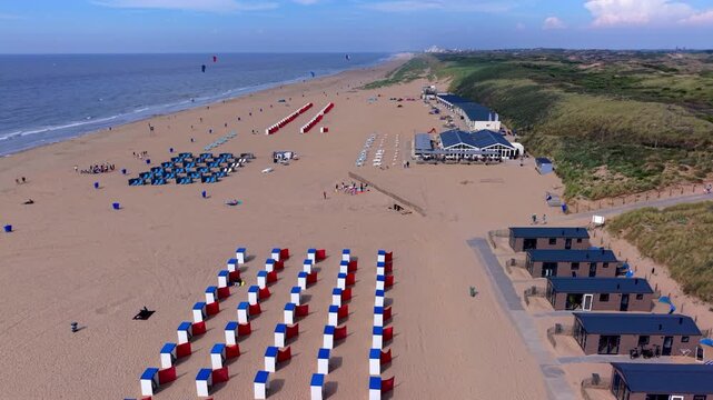 Aerial view video clip of Katwijk aan Zee beach resort red white blue beach cabins, wooden holiday bungalows, beach chairs, coastal dunes, and North Sea shore in South Holland