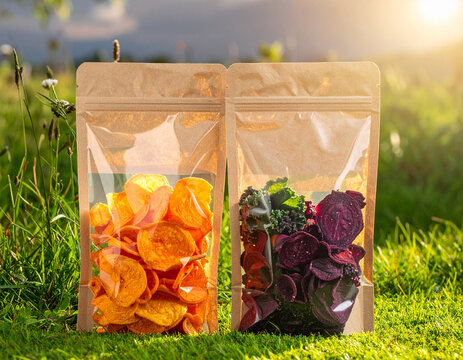 Translucent snack boxes made from cornstarch-based bioplastic are filled with veggie chips and sit on a bright green lawn.