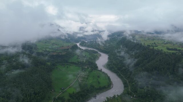 Aerial view of a wide muddy river cutting between a large green fertile patch and steep forested banks in Nepal