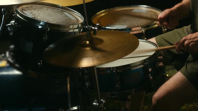 Close up view of a musician playing a rhythmic beat on a drum kit with wooden sticks, hitting the snare drum and cymbals during a live performance or rehearsal in a studio