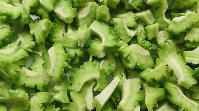 Bitter melon vegetable fruit sliced into small closeup slow spinning motion top view. Pile of organic fresh raw bitter gourd cut pieces stacked. Healthy antioxidant alternative diet lifestyle concept.