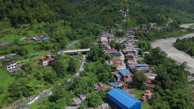 Closer aerial shot over a riverside town showing colorful rooftops, a bridge crossing a tributary, and a main muddy river in Nepal