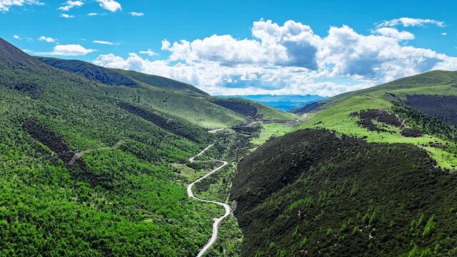 Aerial view of a scenic winding road passing through a lush green mountain valley under a blue sky in Western Sichuan, China