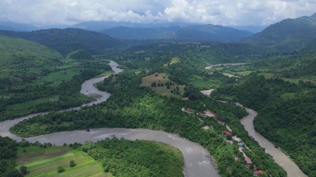 Aerial establishing shot of a meandering muddy river passing through agricultural fields and mountain valleys in Nepal