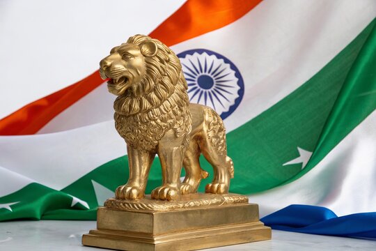 Golden lion statue standing proudly before waving Indian tricolor flag.