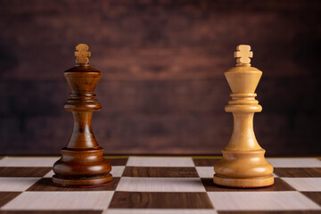 Fototapeta premium Wooden black and white chess king pieces standing face to face on chessboard against dark brown background. Concept of strategy, conflict, leadership, competition, and business duel.