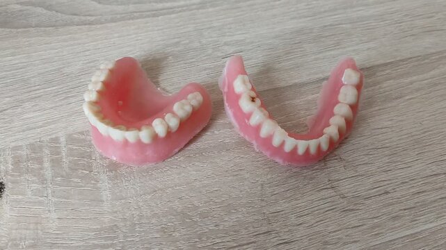 Upper and lower dental dentures with pink gums placed on a wooden table