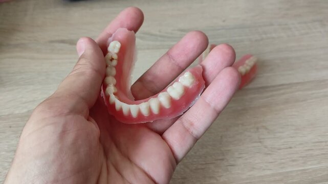 Hand holding a curved pink dental denture with white teeth in focus