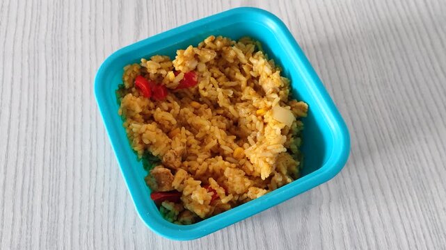 Blue plastic container filled with spiced rice, chicken and bell peppers top view