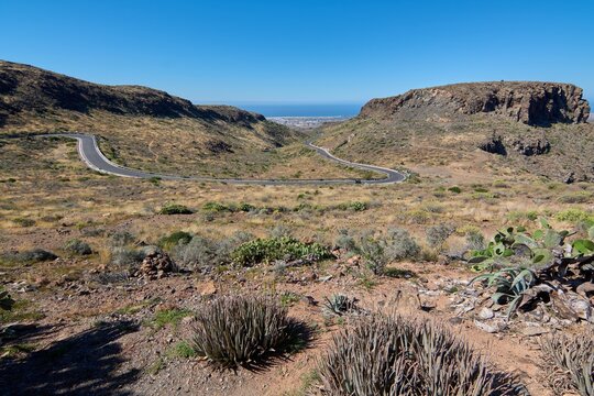 Wide-angle landscape view of the winding mountain highway and rugged terrain of Degollada las Yeguas under a bright blue sky in Gran Canaria.