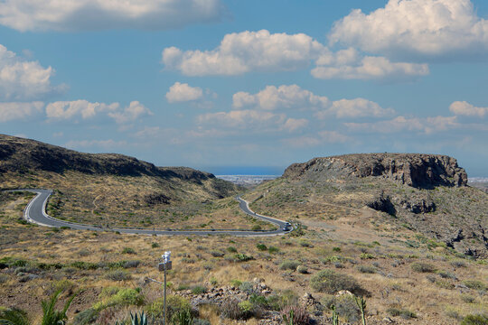Scenic view of the winding mountain highway and arid valley of Degollada las Yeguas under a partly cloudy sky with distant ocean in Gran Canaria.