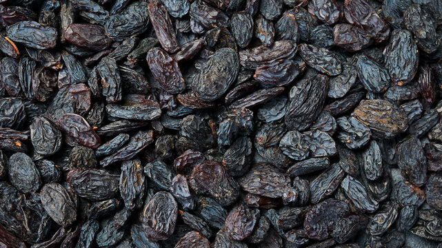 Dark dried raisins fill the entire frame creating a textured background. Delicious sweet fruits are rich in vitamins. Perfect picture for healthy eating concepts.