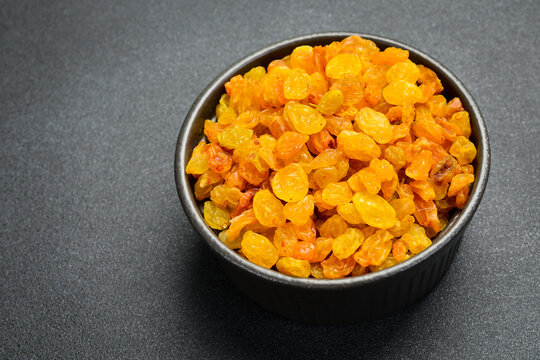 Golden dried raisins fill a round bowl placed on a grey slate background. Sweet organic fruits are rich in vitamins. Healthy food concept with copy space.