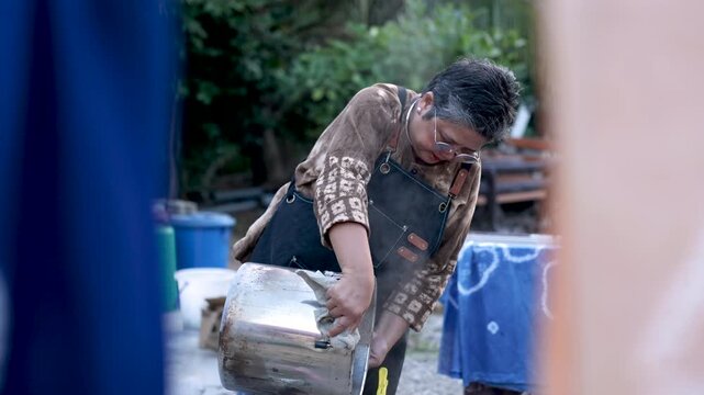 Retired small business owner filtering steaming dye outdoors, textile craft production, artisan skill, active retirement, independent work, productive aging lifestyle business work.
