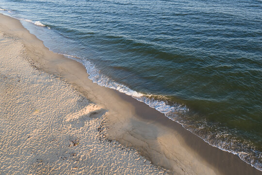 Aerial view of calm sea waves rolling onto a golden sandy coastline at Perakula beach in Nova Estonia during warm morning sunlight.