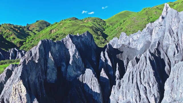 Aerial view of sharp gray rock formations and green hills under a clear blue sky in Moshi Park, Garze, Sichuan, China
