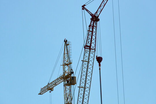 Cranes are lifting materials at a construction site in the city. The building work is ongoing under bright blue skies