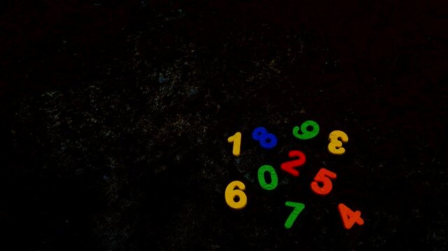Set of multi colored plastic toy numbers scattered on dark textured background colorful math