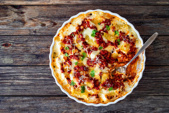 Bolognese pasta casserole - baked rigatoni noodles with bolognese sauce, mozzarella cheese and b&eacute;chamel sauce on wooden table. Top view
