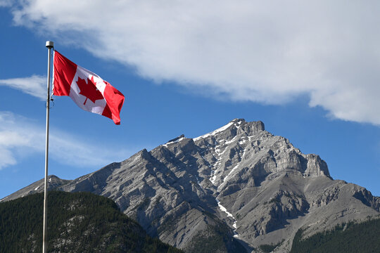 Canadian flag against the sky and a mountain in the background. Canada