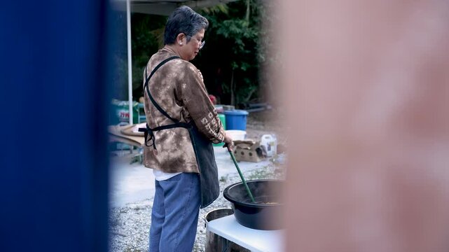 Healthy retired woman working beside steaming dye bath outdoors, handmade tie dye production, artisan skill, small business routine, productive aging, independent creative lifestyle.