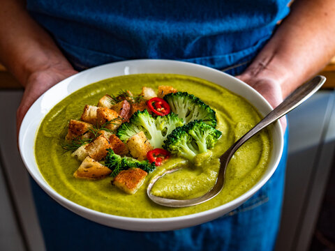 Woman holding plate with cream broccoli soup 
