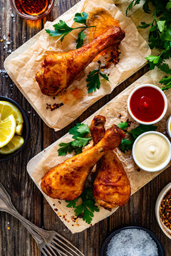 Air fryer chicken drumsticks with mayonnaise, ketchup and mustard on wooden table. Top view

