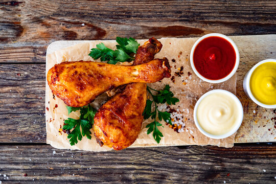 Air fryer chicken drumsticks with mayonnaise, ketchup and mustard on wooden table. Top view

