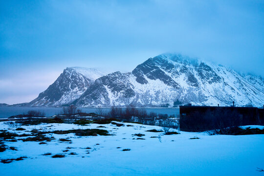 Stunning winter landscape of Lofoten islands in Norway during sunset. Beautiful scenic view of snow-capped mountains and sea under a warm soft evening sky in Arctic Scandinavia.