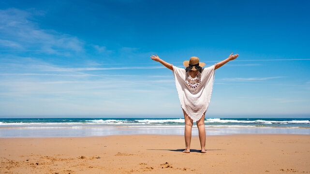 Beautiful middle-aged woman enjoying walk on sunny sandy paradise beach in summertime. Back view
