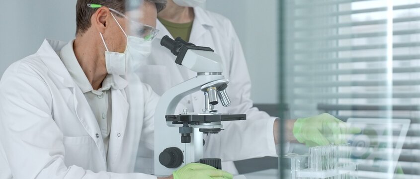 Scientific team analyzing samples in a modern laboratory, focusing on research and development for health care solutions, using advanced microscopes and digital data for discovery and progress