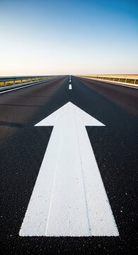 Low angle view of a crisp white arrow painted on dark asphalt, pointing forward along a straight road toward success and future goals, pointer, infrastructure, empty