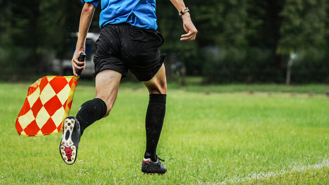 Assistant referee running with checkered flag during outdoor football match on grass field